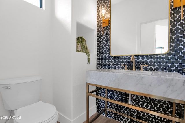 bathroom featuring a sink, toilet, tasteful backsplash, wood finished floors, and baseboards