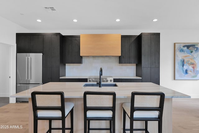 kitchen with high quality fridge, dark cabinets, light wood-style flooring, a sink, and visible vents