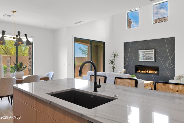 kitchen with a sink, a wealth of natural light, hanging light fixtures, and light stone counters