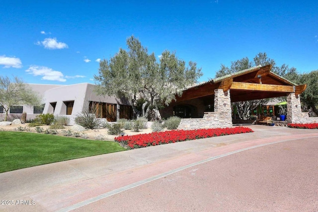 view of front of house featuring stone siding, an attached carport, stucco siding, and a front lawn