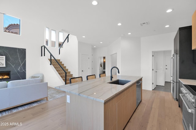 kitchen featuring light wood-style flooring, modern cabinets, a sink, high end appliances, and open floor plan
