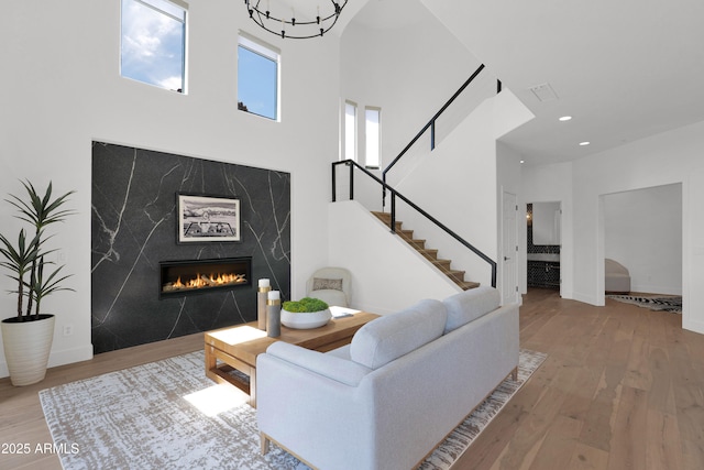 living area with recessed lighting, a high end fireplace, wood finished floors, stairway, and a high ceiling