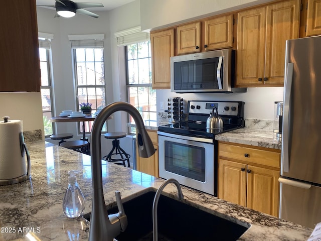 kitchen with appliances with stainless steel finishes, a ceiling fan, and light stone countertops