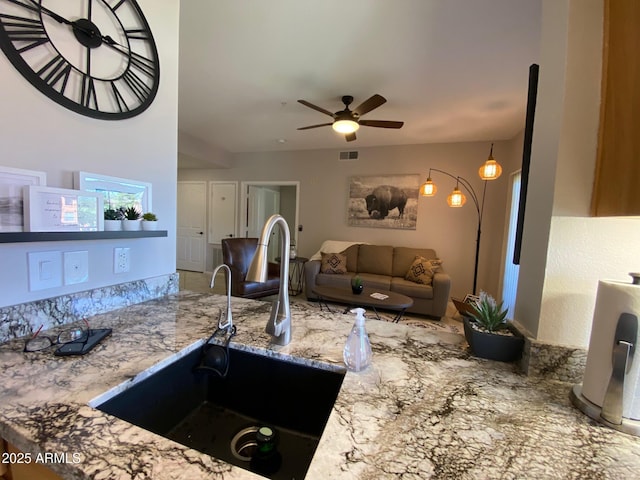 kitchen with a sink, ceiling fan, and light stone countertops