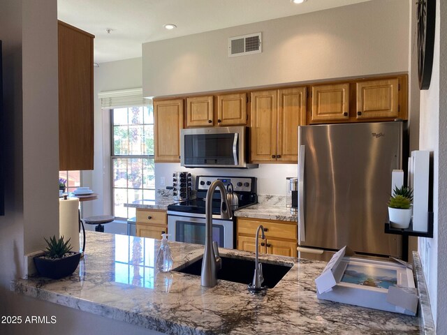 kitchen with appliances with stainless steel finishes, light stone counters, and a peninsula