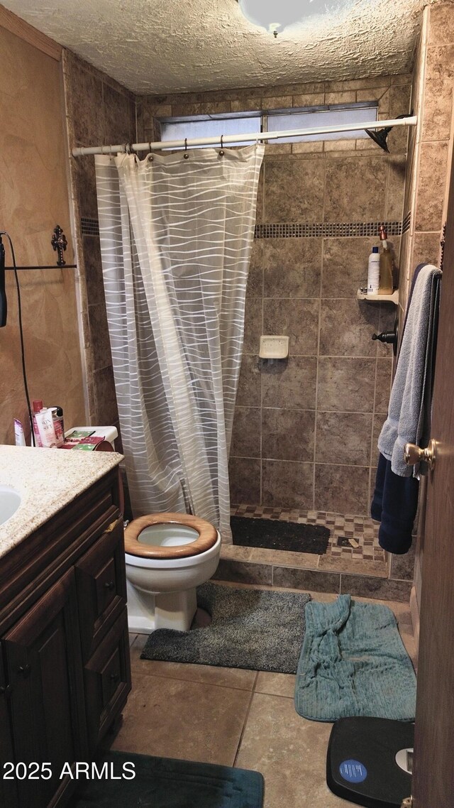 bathroom with vanity, toilet, a tile shower, and a textured ceiling