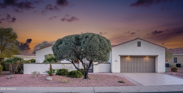 view of front of house featuring a garage, concrete driveway, central AC unit, and stucco siding