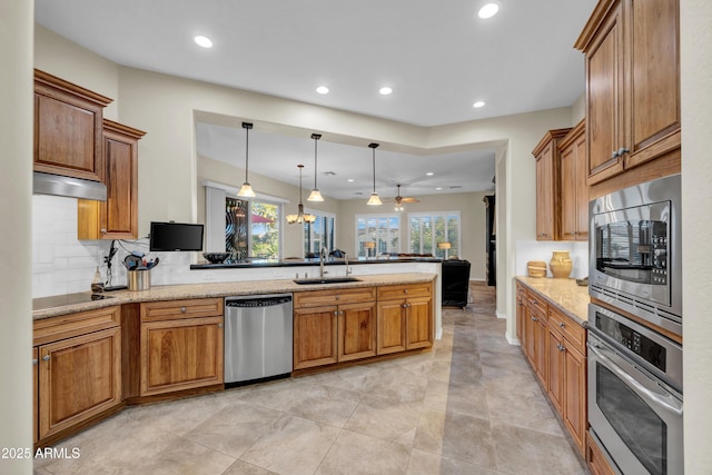 kitchen with stainless steel appliances, light stone counters, a sink, and decorative light fixtures