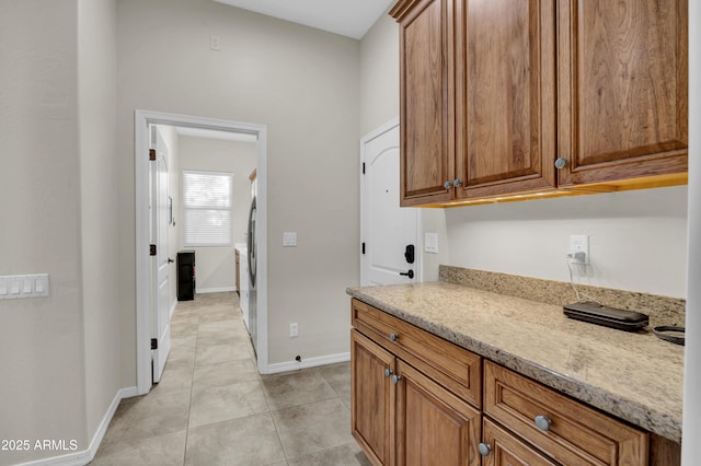 kitchen with baseboards, light stone counters, light tile patterned flooring, and brown cabinets