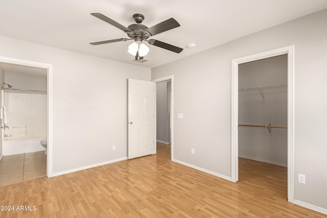 unfurnished bedroom featuring a spacious closet, ensuite bathroom, light hardwood / wood-style floors, and ceiling fan