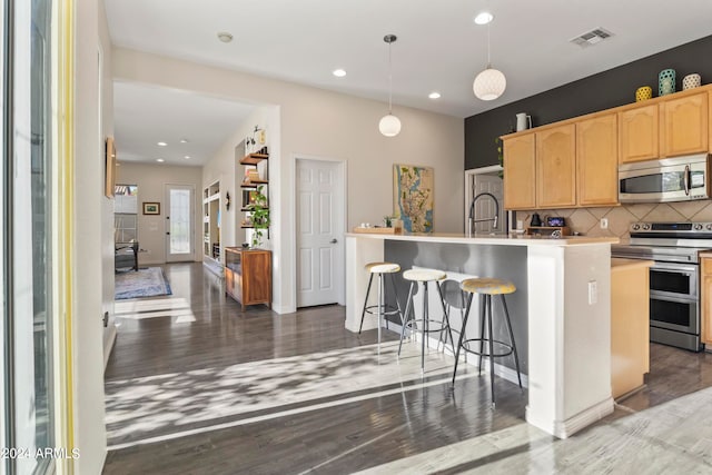 kitchen with backsplash, stainless steel appliances, a kitchen island with sink, hardwood / wood-style flooring, and hanging light fixtures