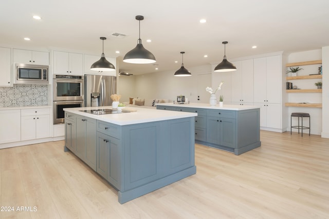 kitchen with a kitchen island with sink, appliances with stainless steel finishes, white cabinets, and pendant lighting