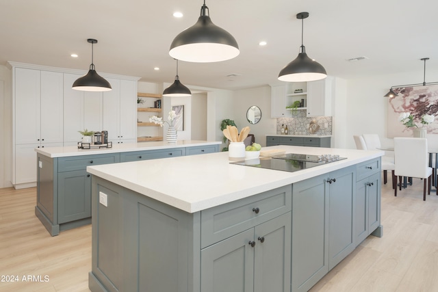 kitchen with hanging light fixtures, light wood-type flooring, black electric cooktop, a kitchen island, and tasteful backsplash