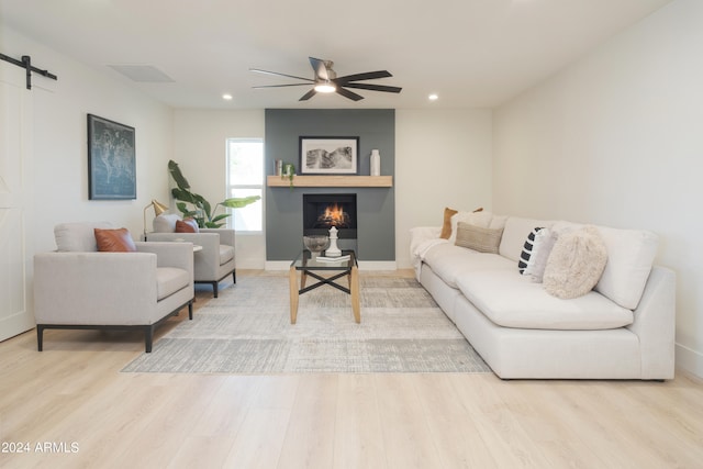 living room featuring ceiling fan, a barn door, and light hardwood / wood-style floors