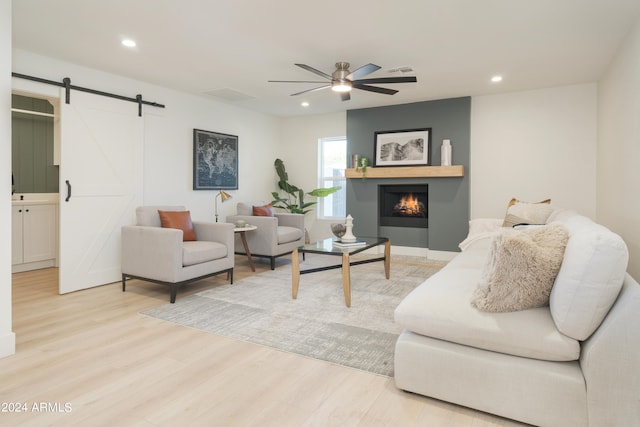 living room featuring light hardwood / wood-style flooring, ceiling fan, and a barn door