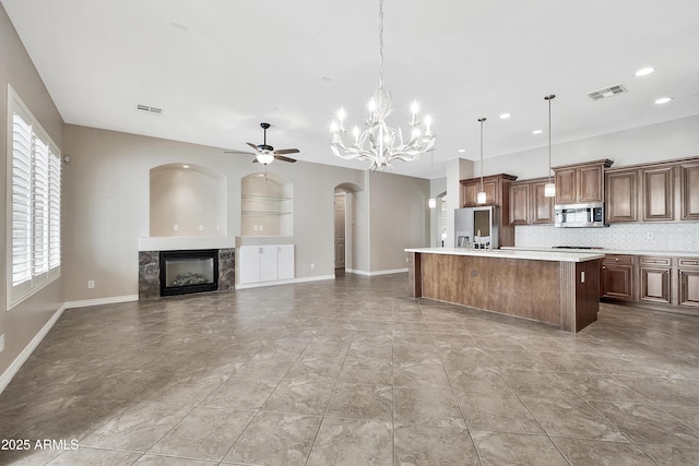 kitchen featuring visible vents, a kitchen island with sink, ceiling fan with notable chandelier, stainless steel appliances, and a fireplace