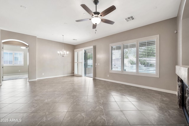 unfurnished living room featuring visible vents, baseboards, ceiling fan with notable chandelier, a fireplace, and arched walkways