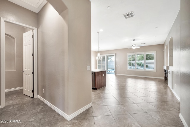 hall featuring light tile patterned flooring, baseboards, visible vents, and arched walkways