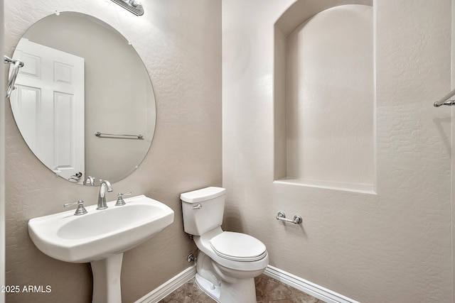 bathroom with toilet, a textured wall, baseboards, and a sink