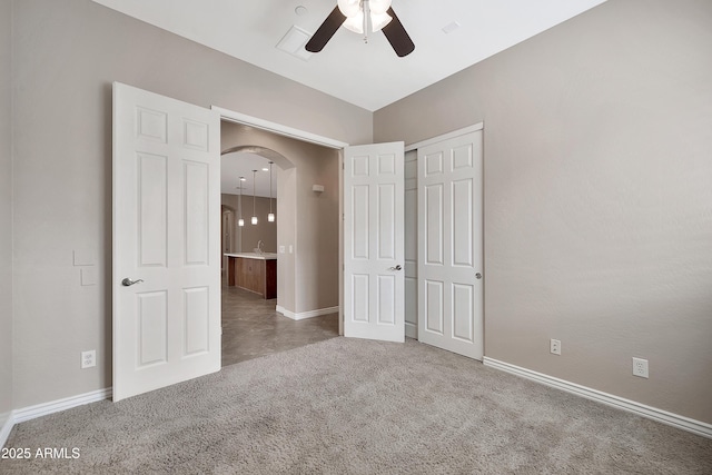 unfurnished bedroom featuring carpet, arched walkways, a closet, and baseboards