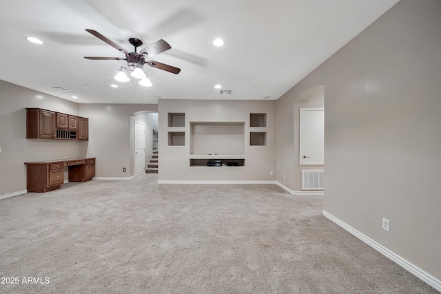 unfurnished living room featuring visible vents, arched walkways, light colored carpet, and ceiling fan