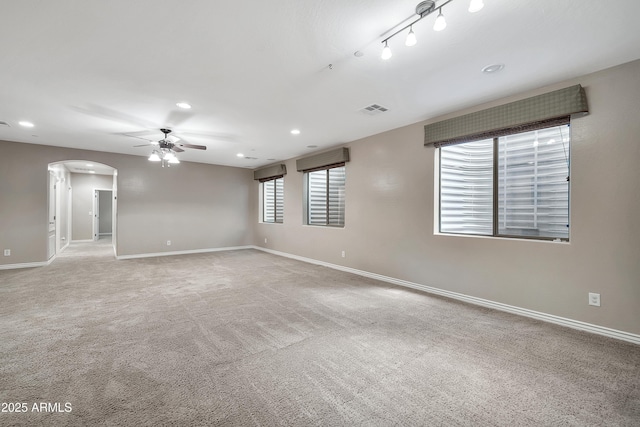 empty room featuring visible vents, baseboards, ceiling fan, carpet flooring, and arched walkways