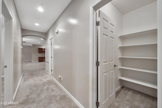 hallway featuring arched walkways, recessed lighting, light colored carpet, and baseboards