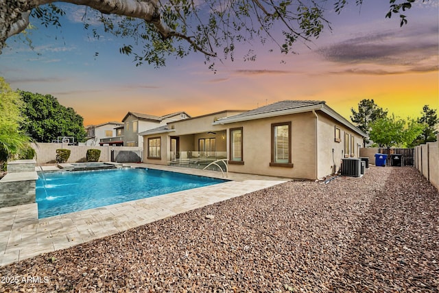 pool at dusk with central air condition unit, a fenced backyard, a fenced in pool, an in ground hot tub, and a patio area