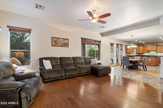 living room featuring light wood-style floors, visible vents, ceiling fan with notable chandelier, and recessed lighting