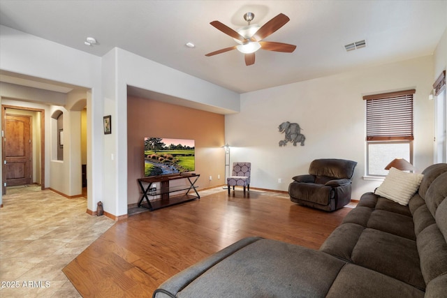 living room with light wood-type flooring, visible vents, baseboards, ceiling fan, and arched walkways