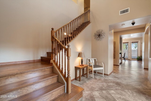 stairway with a towering ceiling, baseboards, and visible vents