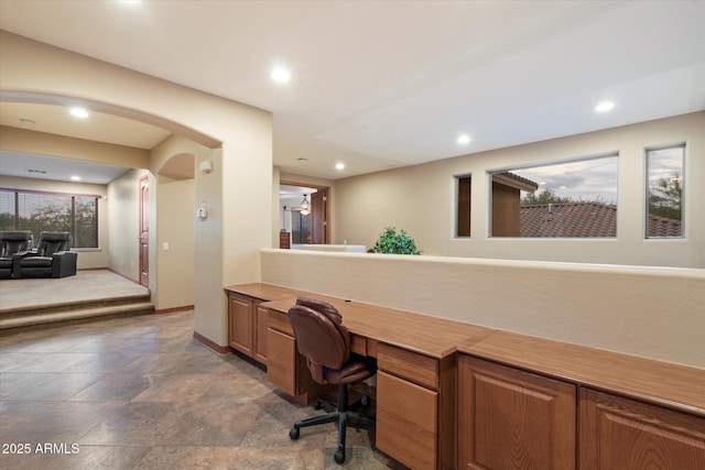 office space with built in study area, stone finish floor, recessed lighting, arched walkways, and baseboards