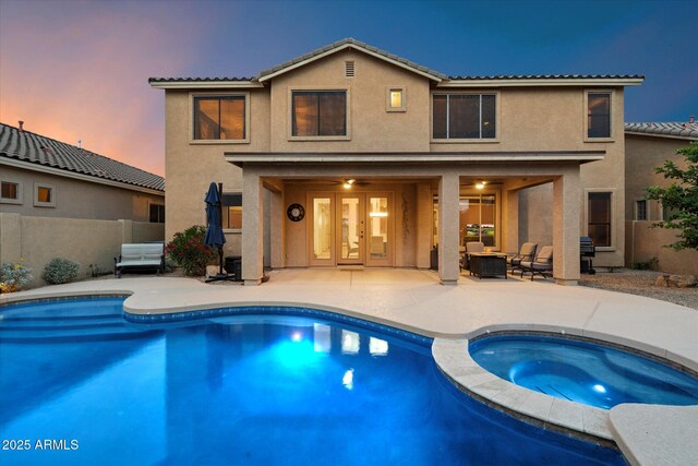 back of house at dusk featuring a tile roof, a patio, and stucco siding