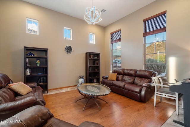 living area with an inviting chandelier, light wood-style flooring, a high ceiling, and visible vents