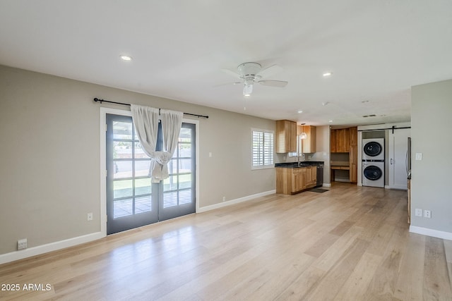3138 N 82nd Pl, Scottsdale, AZ 85251 - unfurnished living room featuring ceiling fan, a barn door, stacked washing maching and dryer, light wood finished floors, and baseboards