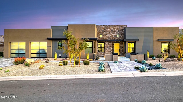 contemporary home with stone siding, decorative driveway, an attached garage, and stucco siding