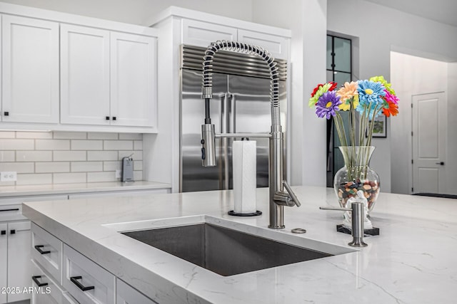 kitchen with built in refrigerator, tasteful backsplash, light stone counters, and white cabinets