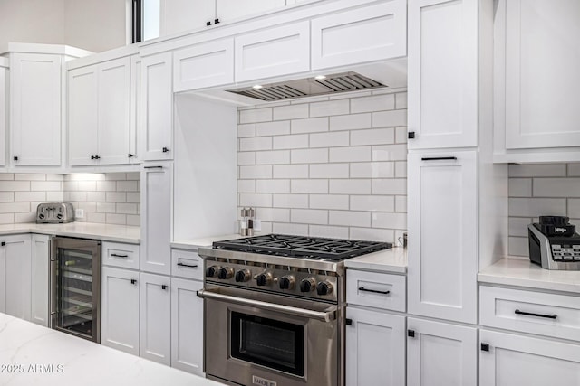 kitchen featuring wine cooler, stainless steel stove, white cabinets, backsplash, and light stone countertops