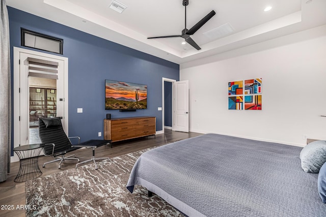 bedroom featuring a tray ceiling, visible vents, baseboards, and wood finished floors