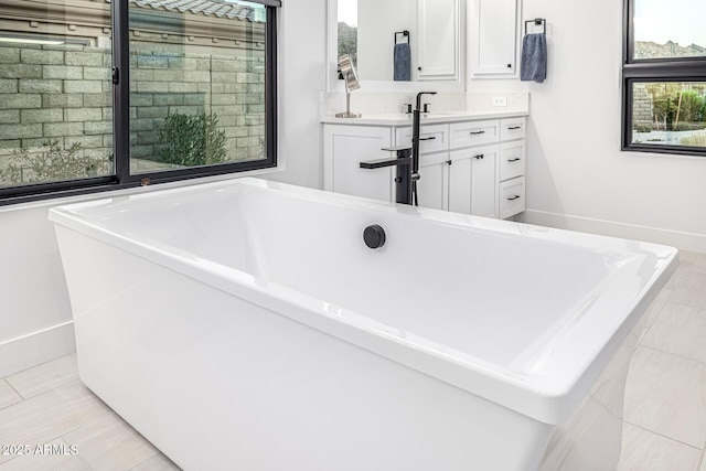 full bathroom with a freestanding bath, tile patterned flooring, vanity, and baseboards