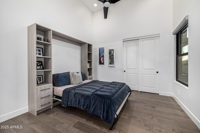 bedroom with dark wood-style floors, a high ceiling, baseboards, and a closet