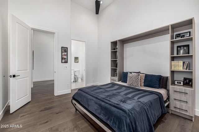 bedroom featuring ensuite bath, a towering ceiling, baseboards, and wood finished floors