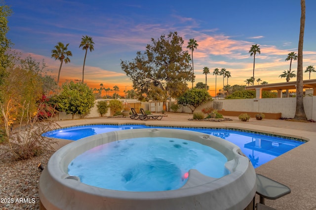 pool at dusk featuring a patio area and an outdoor hot tub