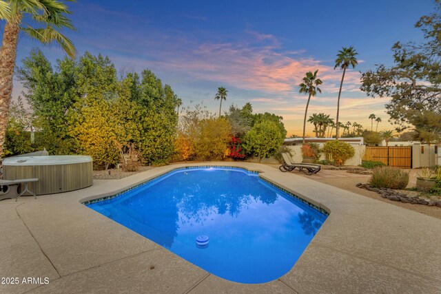 pool at dusk with a patio and a hot tub