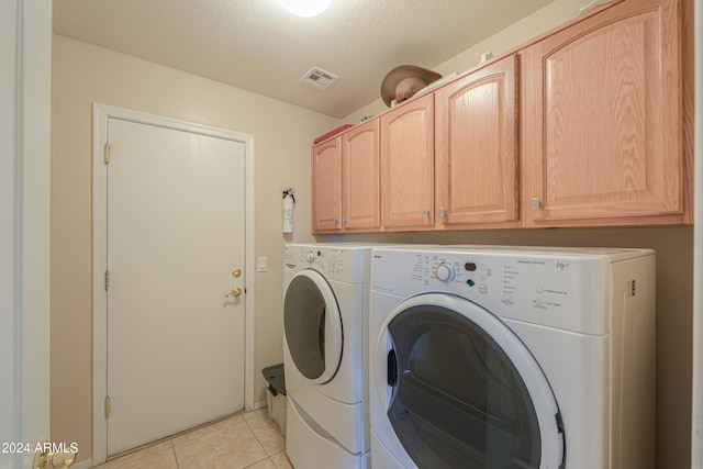 washroom with washing machine and dryer, light tile patterned floors, cabinets, and a textured ceiling