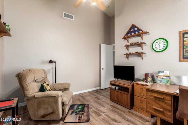 sitting room featuring ceiling fan, light hardwood / wood-style flooring, and a towering ceiling