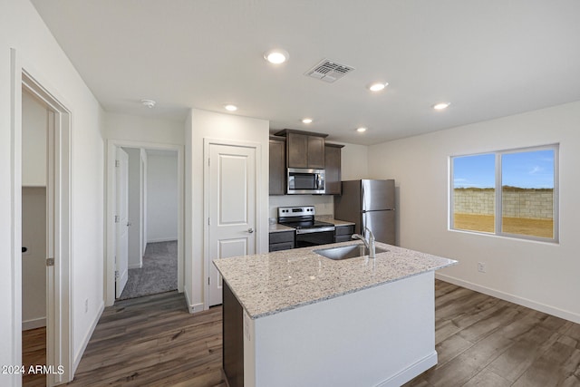 kitchen with dark wood-type flooring, an island with sink, appliances with stainless steel finishes, light stone counters, and dark brown cabinetry