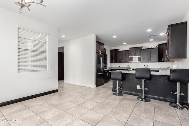 kitchen with stainless steel microwave, freestanding refrigerator, recessed lighting, a peninsula, and light tile patterned floors