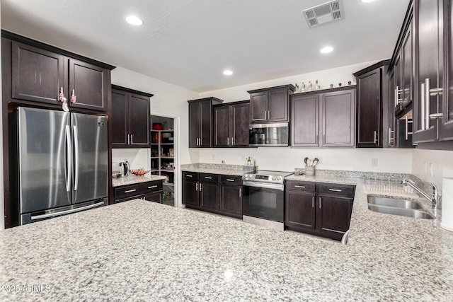 kitchen with appliances with stainless steel finishes, a sink, dark brown cabinets, recessed lighting, and light stone countertops