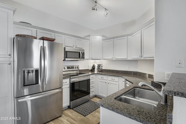 kitchen featuring dark stone countertops, sink, light hardwood / wood-style flooring, appliances with stainless steel finishes, and white cabinets